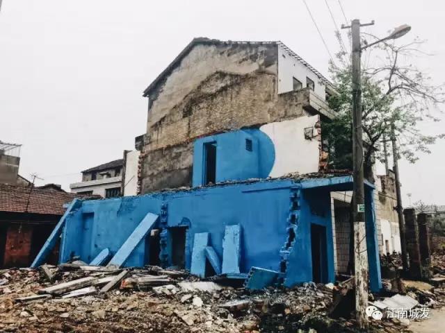 △ 這棟建筑是臨江最近的半拆遷建筑物的遺留，沅江和堤壩成為了展覽的天然背景。創(chuàng)作團隊對這棟建筑進行了半涂裝，將符號性的沅水曲線與拆遷進行中的建筑立面進行意義的疊造，它們共同觸發(fā)了場所空間多元語境的生成，把拆遷這種暫時破壞性、干擾性的介入行動與沅水右岸發(fā)展的未來性、美好性緊密融合。